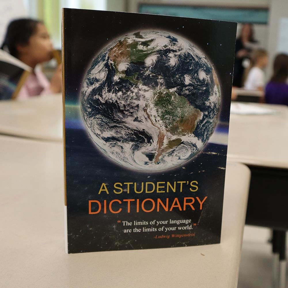  A Student's Dictionary sitting on a desk with students in the background in a classroom